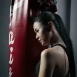 A woman is leaning against a boxing bag.