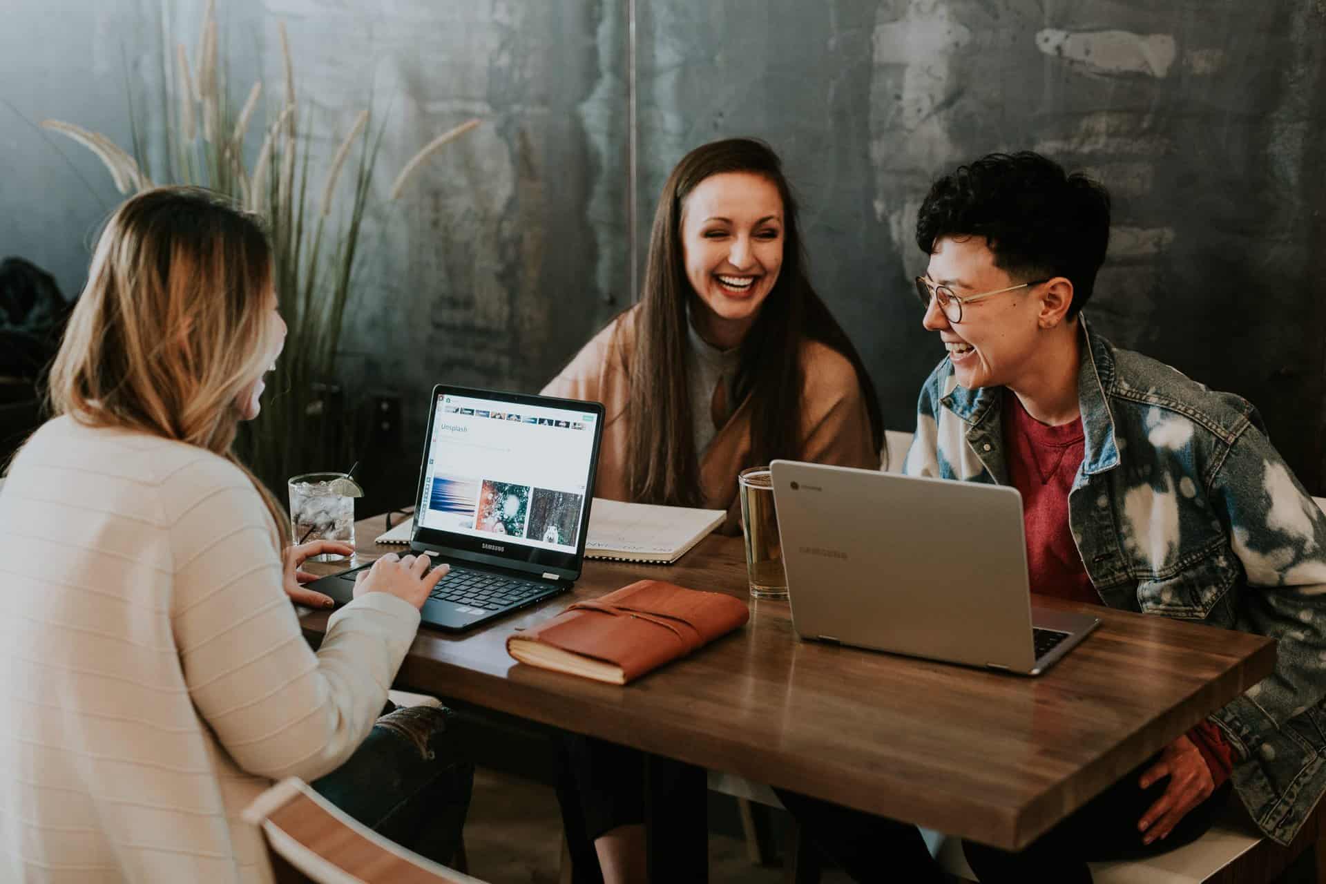 Three women sitting around a table with laptops.