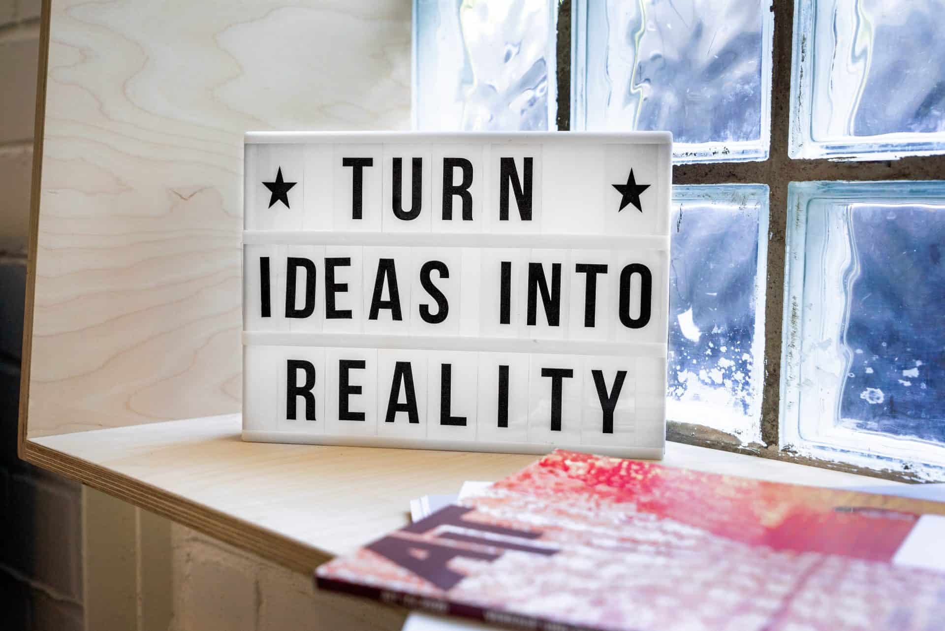 A sign that says turn ideas into reality on a window sill.